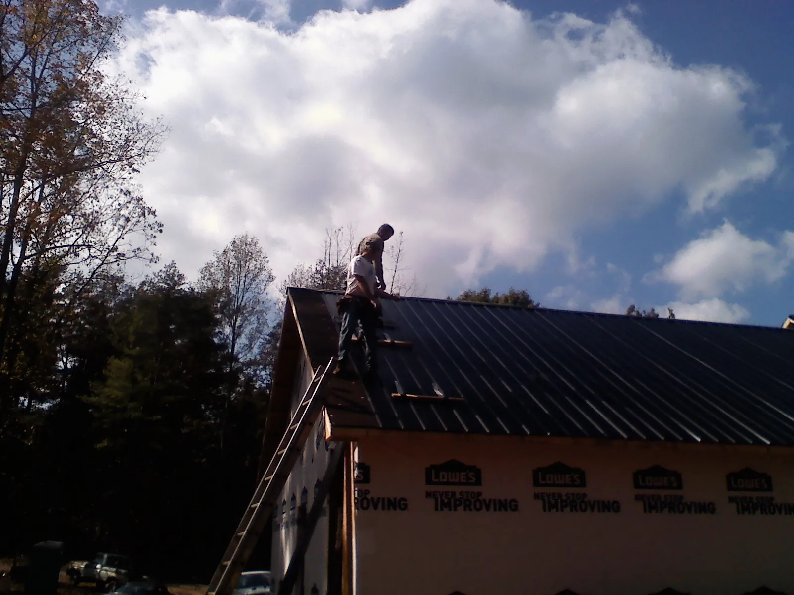 Roofer fastening dark metal panels high against a cloudy sky, from a Roof Inspection job in Titusville